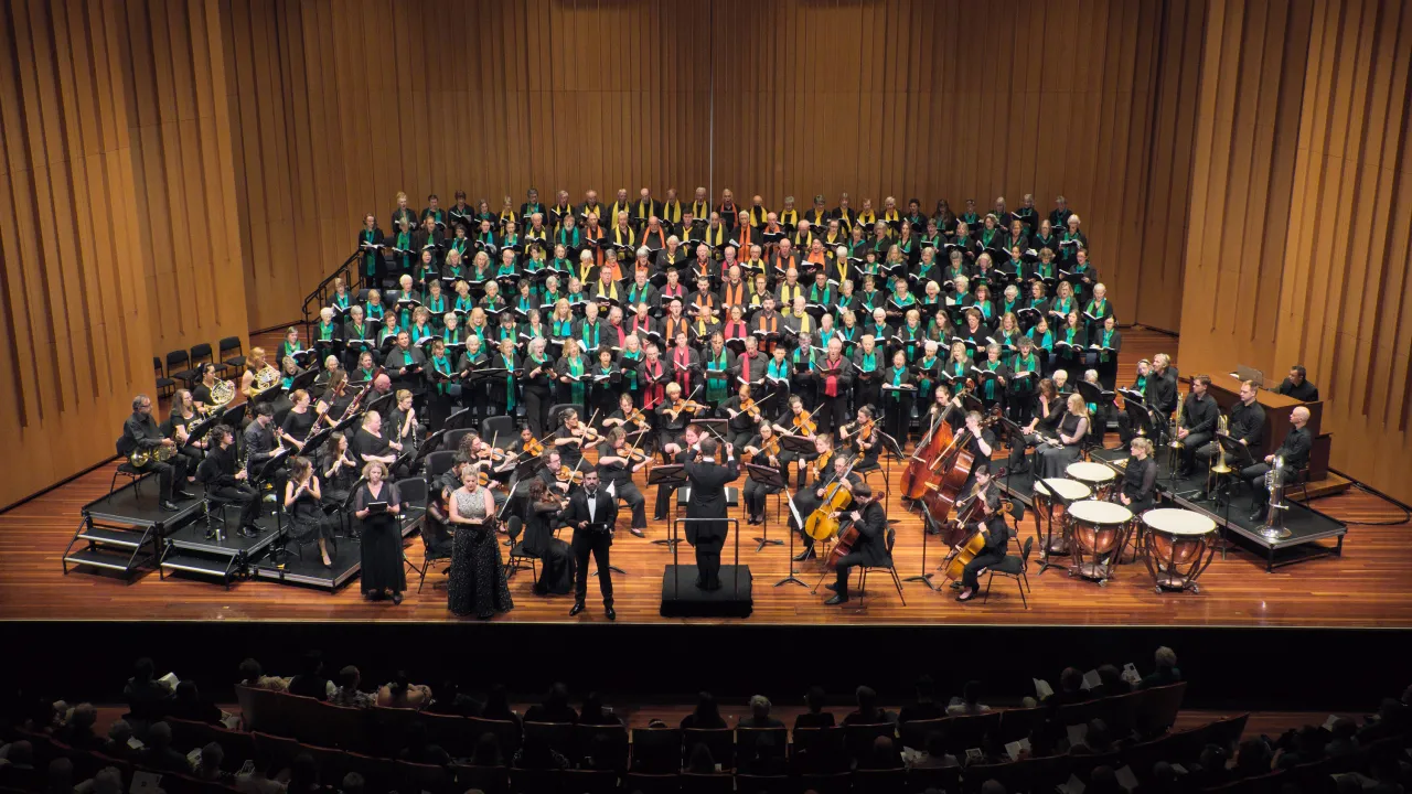 The Canberra Choral Society and National Capital Orchestra perform Mendelssohn’s Elijah at Llewellyn Hall. Conductor Brett Weymark leads the large choir and orchestra, with singers arranged on stage and musicians seated in front, under warm concert lighting.