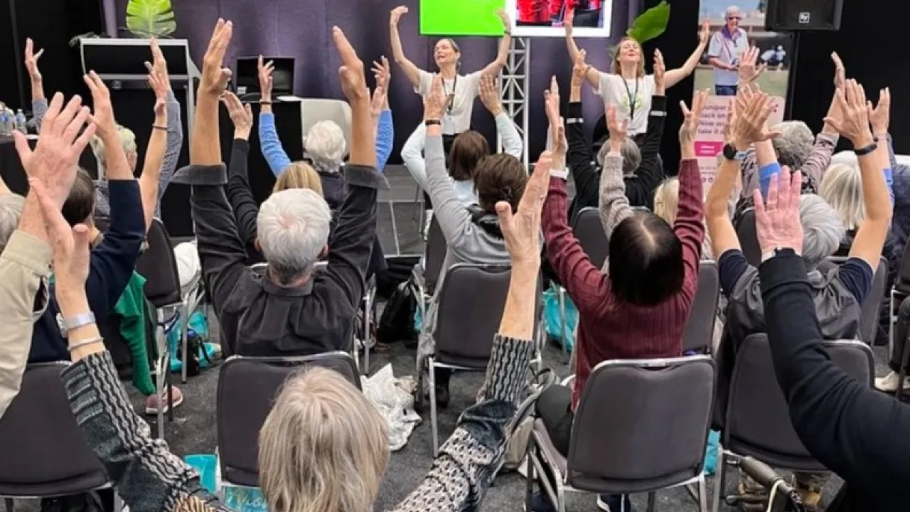 Photo of people sitting in chairs, with hands in the air - in unison, expressing joy.
