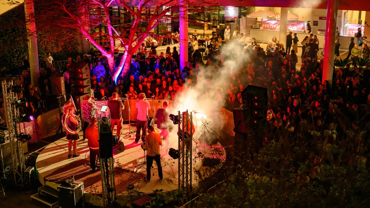 An 8 piece band playing to a crowd on a circular stage at night.