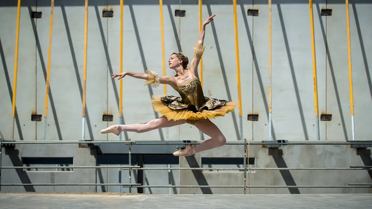 Image of a dancer leaping in front of an industrial backdrop