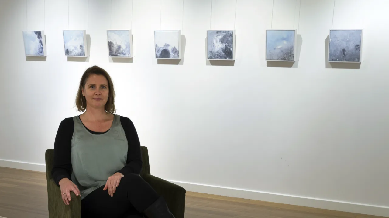 Photograph of artist Amanda Page in a gallery in front of her exhibition of image transfers on the gallery wall.