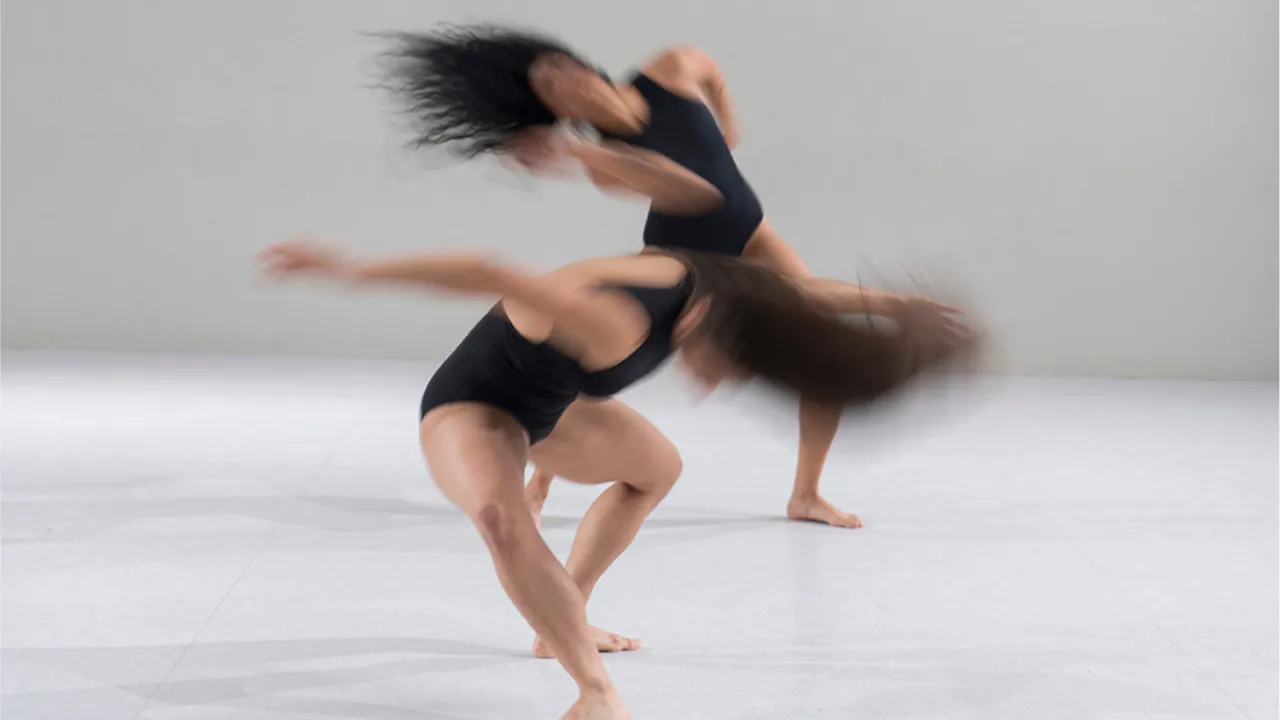 Two dancers feature in a white studio, blurred in a flurry of dynamic movement
