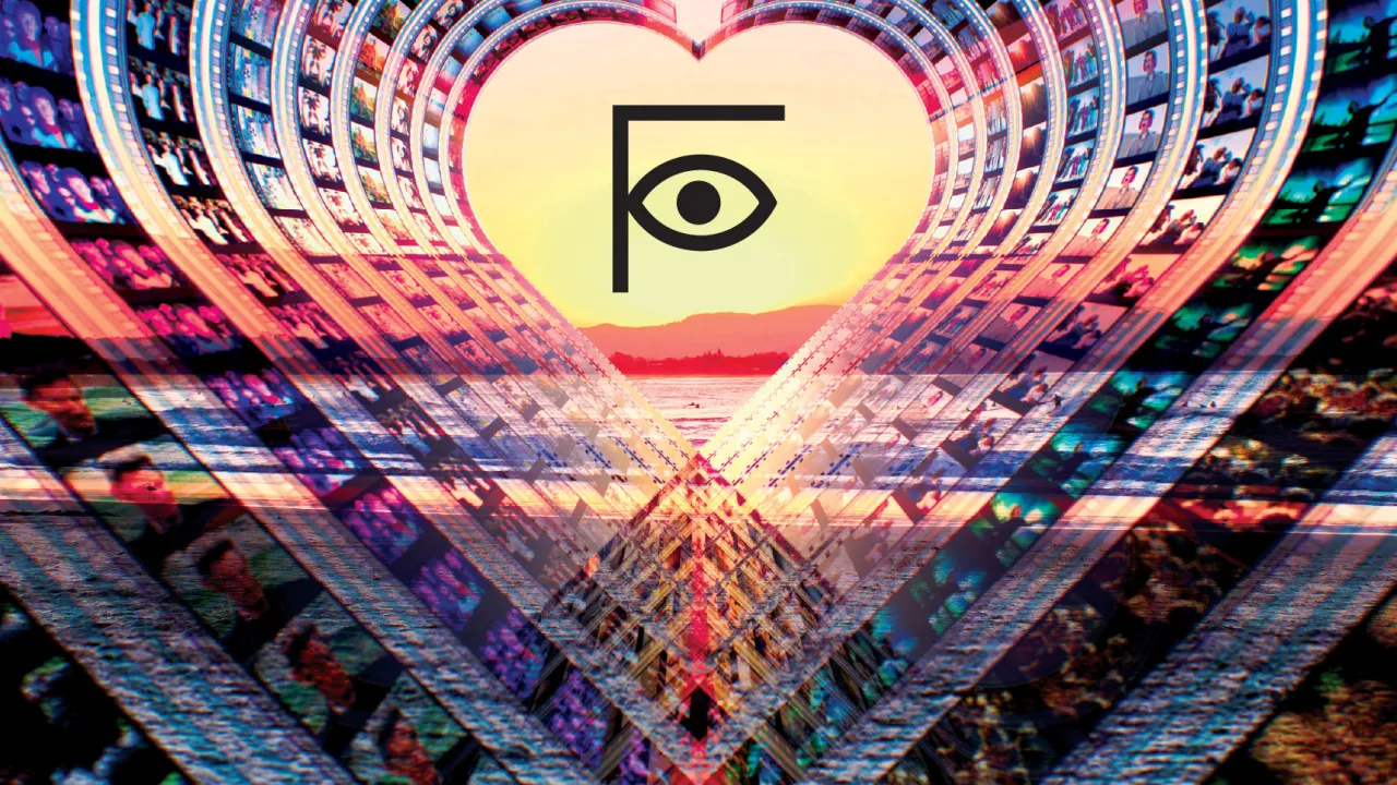 A surreal, colourful digital artwork of film strips curving inward to form a glowing heart shape at the centre. Inside the heart is a stylised eye logo, framed by a radiant sunset sky and reflective water below. The overall design conveys cinema, creativity, and emotional impact.