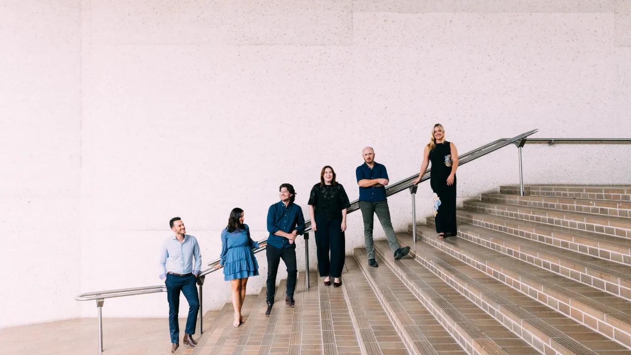 Promotional image for Luminescence Chamber Singers, which shows 6 singers at the National Gallery of Australia