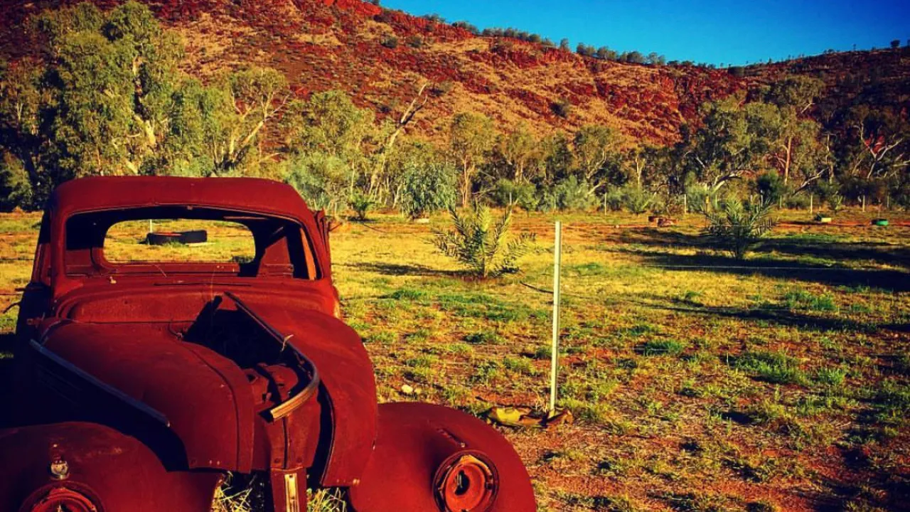 Old beaten up car sitting in a remote regions surrounded by escarpments on red dust.