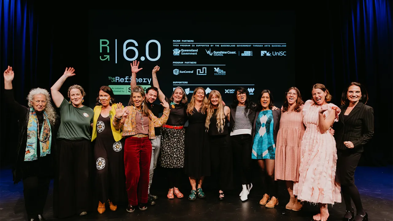 Group of people, male and female standing in front of a board at university with hands up and smiling.