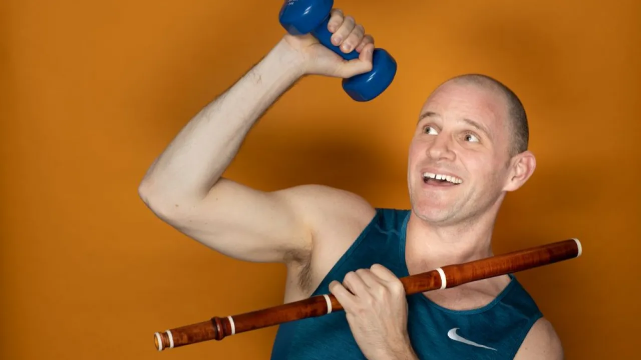 Flautist Andy Skinner holds a baroque flute and a workout weight