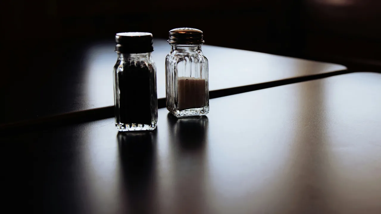 A salt and pepper shaker on a square table in a darkened room