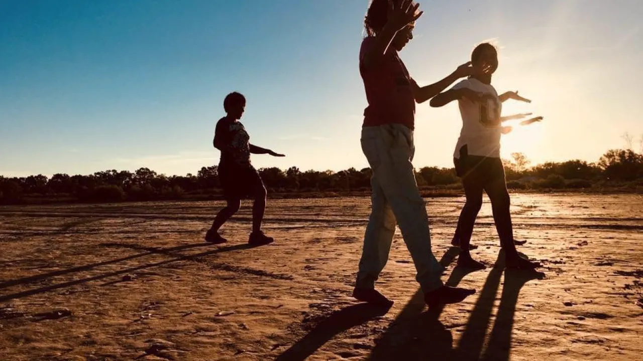 An image of two young people and one dance facilitator moving across the Clay Pans in Wilcannia at sunset