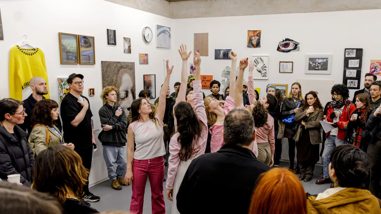 A photo of a circle of dancers facing each other with their arms up in the air. A large crowd surround them watching.