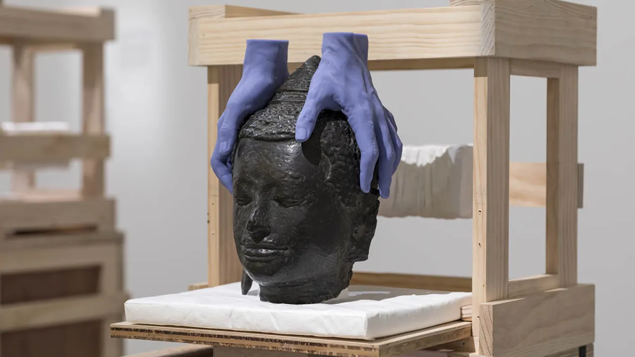 Sculpture of a buddha head with two purple hands holding it