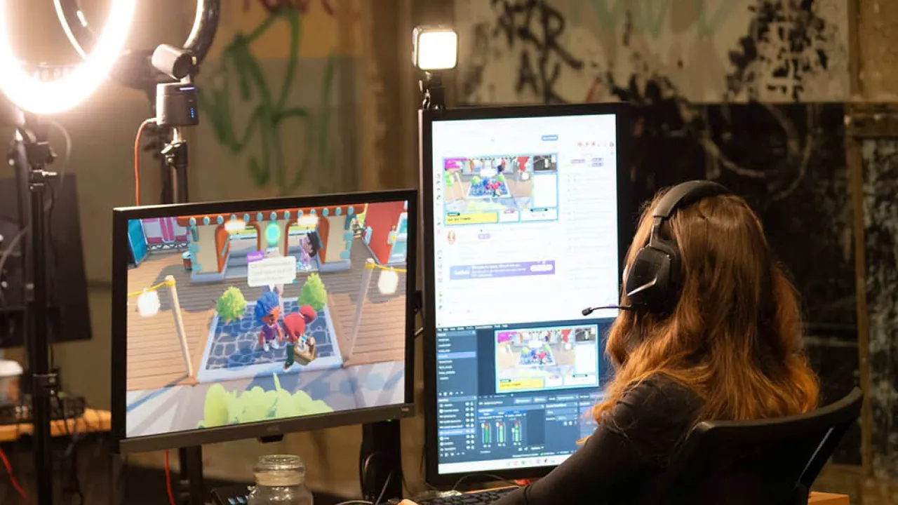 Woman coding a game sitting in front of two monitors