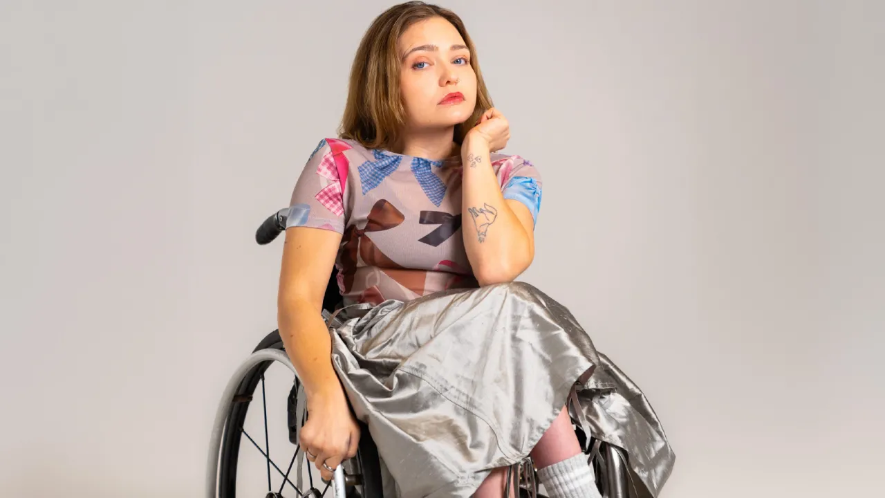 Maya Dove sits in her manual wheelchair wearing a silver skirt and tshirt with bows. 