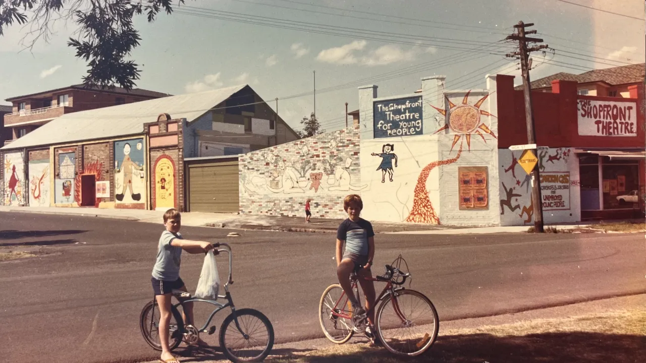 Two kids on bikes in front of Shopfront