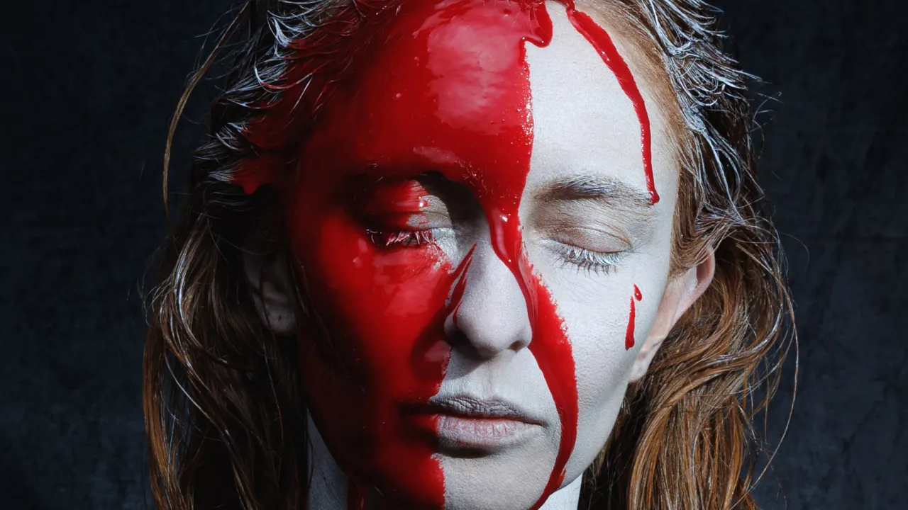 A stark portrait from Thursday’s Child Theatre’s Mary Stuart, depicting a woman with her eyes closed, her face painted white as blood pours over her head, face and body.