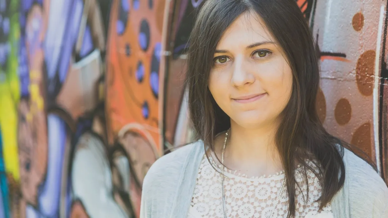 A headshot of Isabella Gerometta, looking at the camera. She is standing in front of a wall of colourful street art.