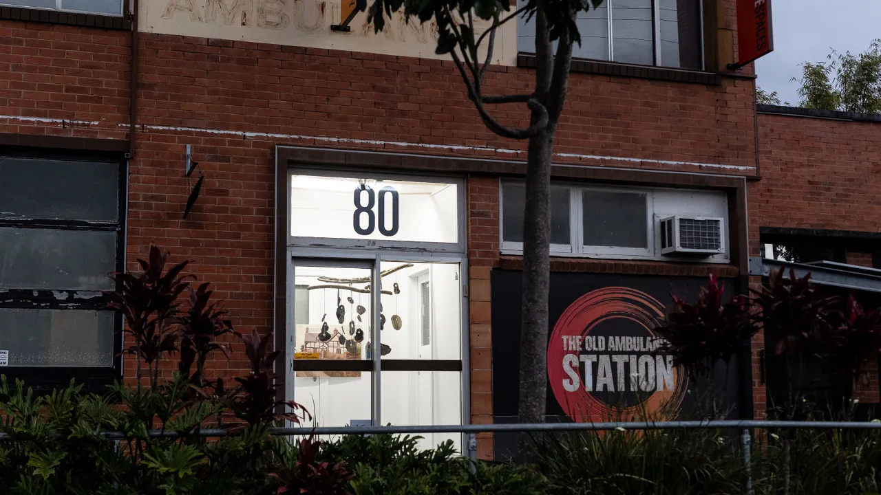 Exterior of a red brick building with a sign that says The Old Ambulance Station. Through the lit window hagstones can be seen hanging from the ceiling as part of an art installation. 