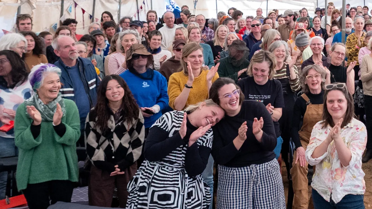 Large group of people wearing colourful tops, smiling and clapping in celebration.