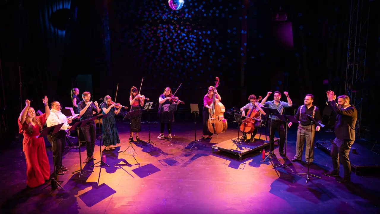 Homophonic! is on stage under a disco ball and great lighting. Strings, Voices, and percussion. 