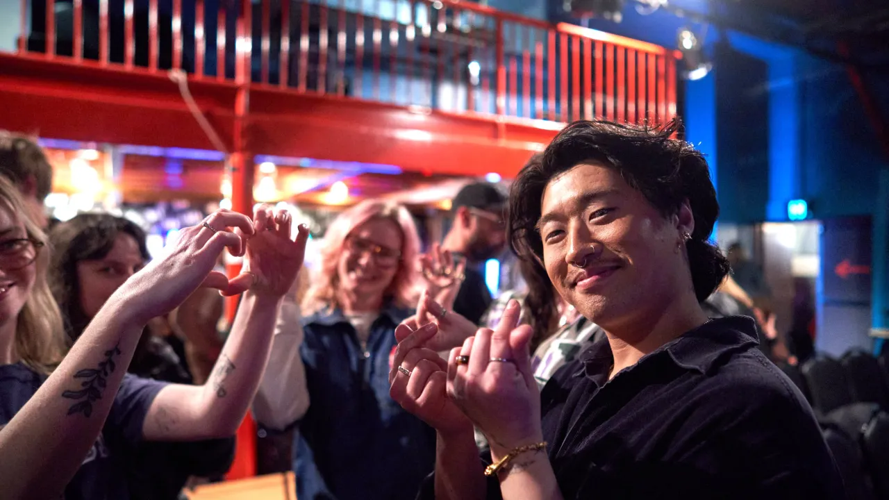 Artist Jake Yang after speaking at SALA Festival's Slide Night, 2026. Jake is standing in a group of friends in a theatre. They are snapping their fingers in congratulations. One person is holding their hands in a love-heart guesture.