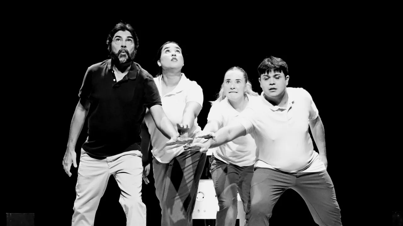  A black and white production photograph from RECALIBRATE by Shock Therapy Arts, featuring 4 artists (left to right: Colin Smith, Keeley Hay, Abigail Waugh and Peter Cook). They have their outstretched hands “all-in” stacked one on top of another, and they look out or up with anticipation.