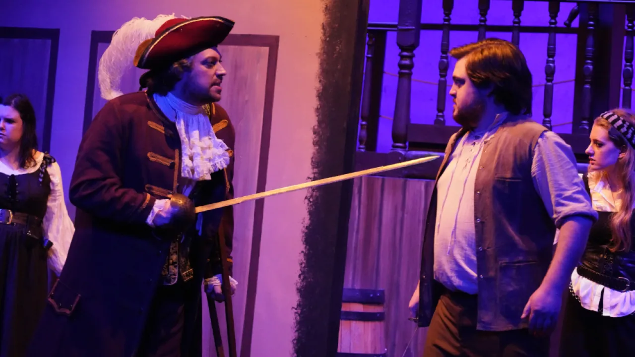 two actors on stage, one (in pirate costume) pointing a sword at the other one