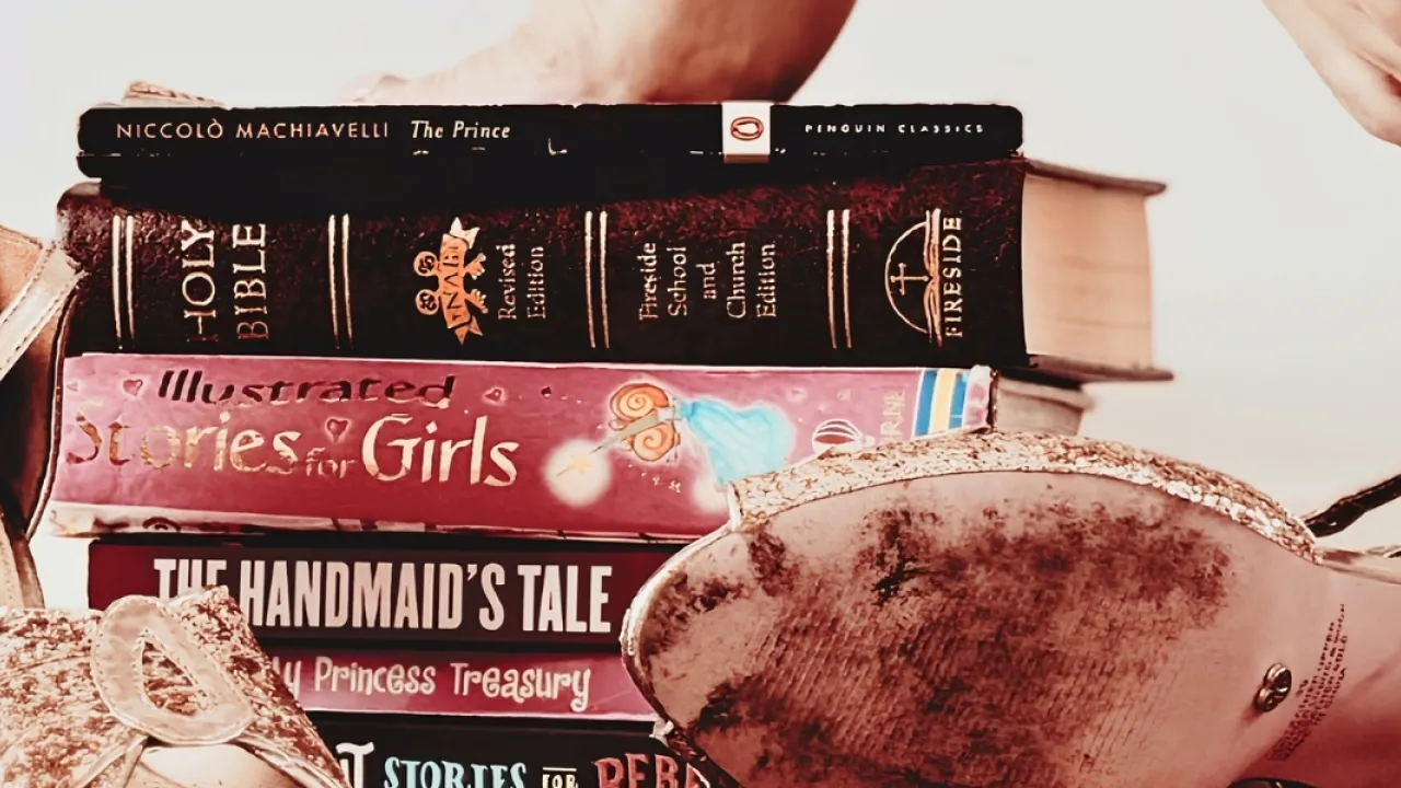 Glittery gold and pink high heels rest discarded beside a stack of books, including "The Prince", "The Children's Bible", "Illustrated Stories for Girls", "The Handmaid’s Tale", "My Princess Treasury" and "Good Night Stories for Rebel Girls". The bare tiptoes of woman can be seen balancing on top of them.