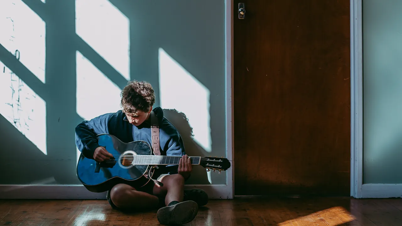 Young boy sitting on the ground practising guitar at Topology's Texas Creative Bootcamp.