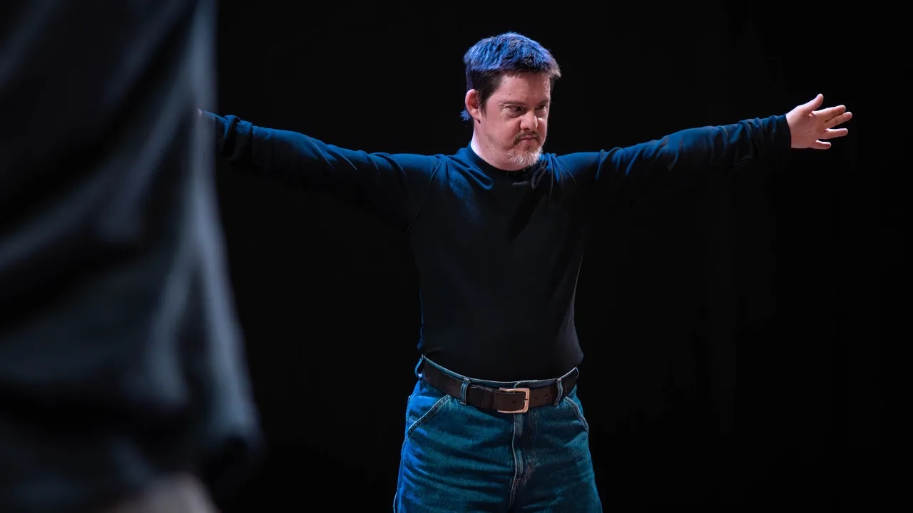 A Rawcus artist stands on stage with their arms outstretched 