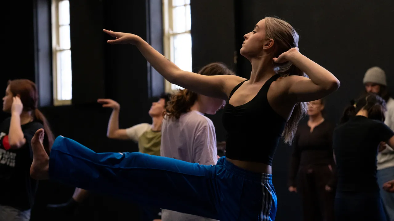 A yound dance artist rehearsing in the theatre with other dancers in the background
