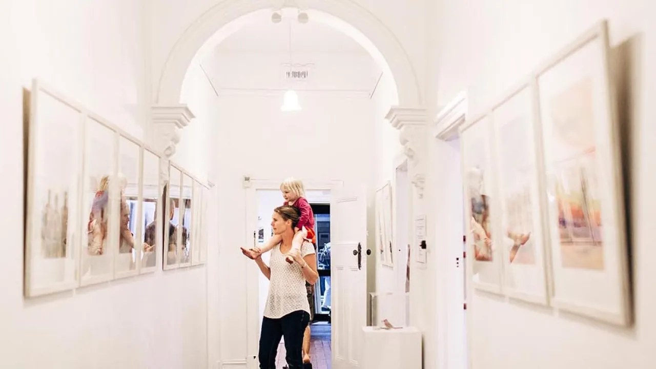 Someone with their child looks at artwork in a white narrow room