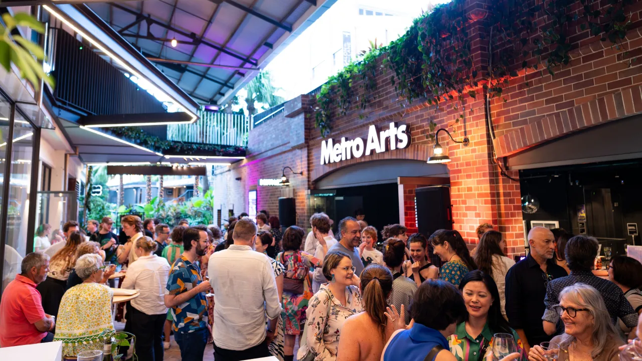 A bright laneway event with many people socialising outside the Metro Arts lobby entry way