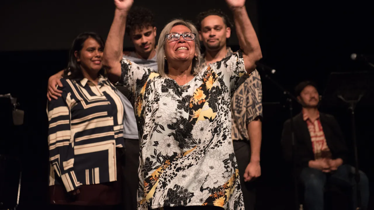 Performer Pamela Young in Steps of the Mighty by H Lawrence Sumner raises both arms triumphantly on stage, smiling as fellow performers gather behind her at Moogahlin Performing Arts’ Yellamundie Festival. Photograph by Jamie James.