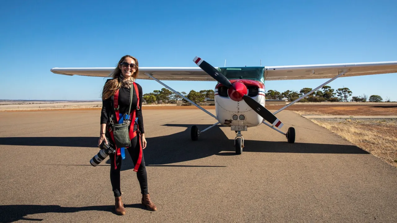 Martine Perret, photographer, stands in front of a plane holding her camera, about to take to the skies to capture aerial photography.