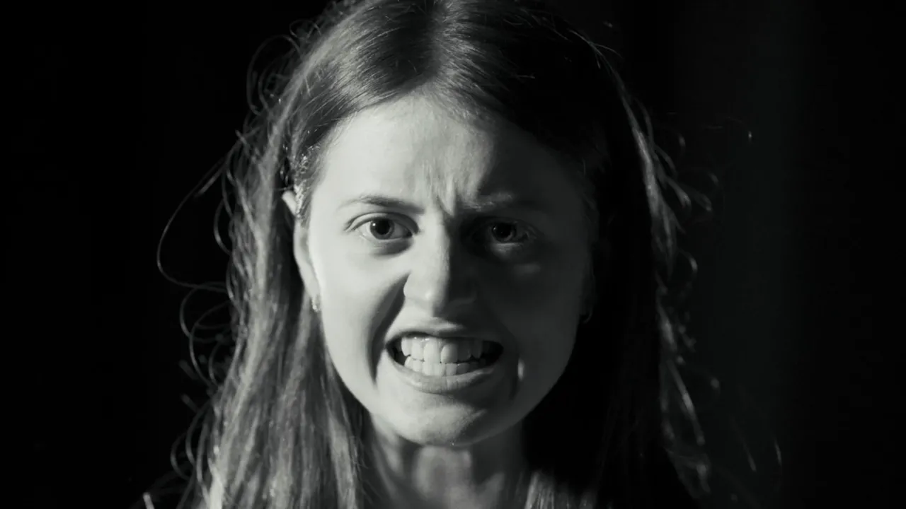 Black and white image of a teenage girl staring at camera, gritting her teeth. 