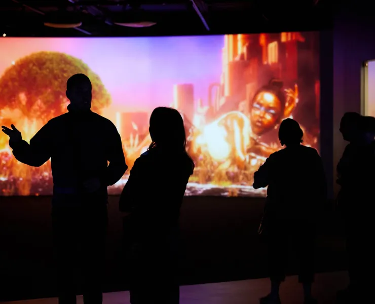 A photo of a large digital screen with the shadows of four people walking past.