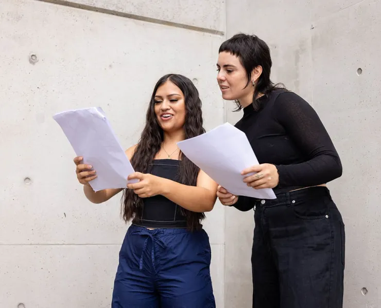 Two women holding scripts in a white room