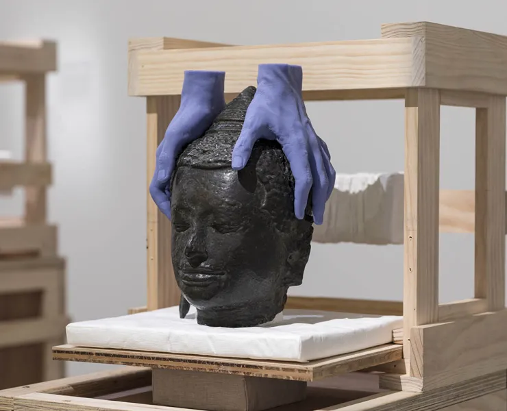 Sculpture of a buddha head with two purple hands holding it