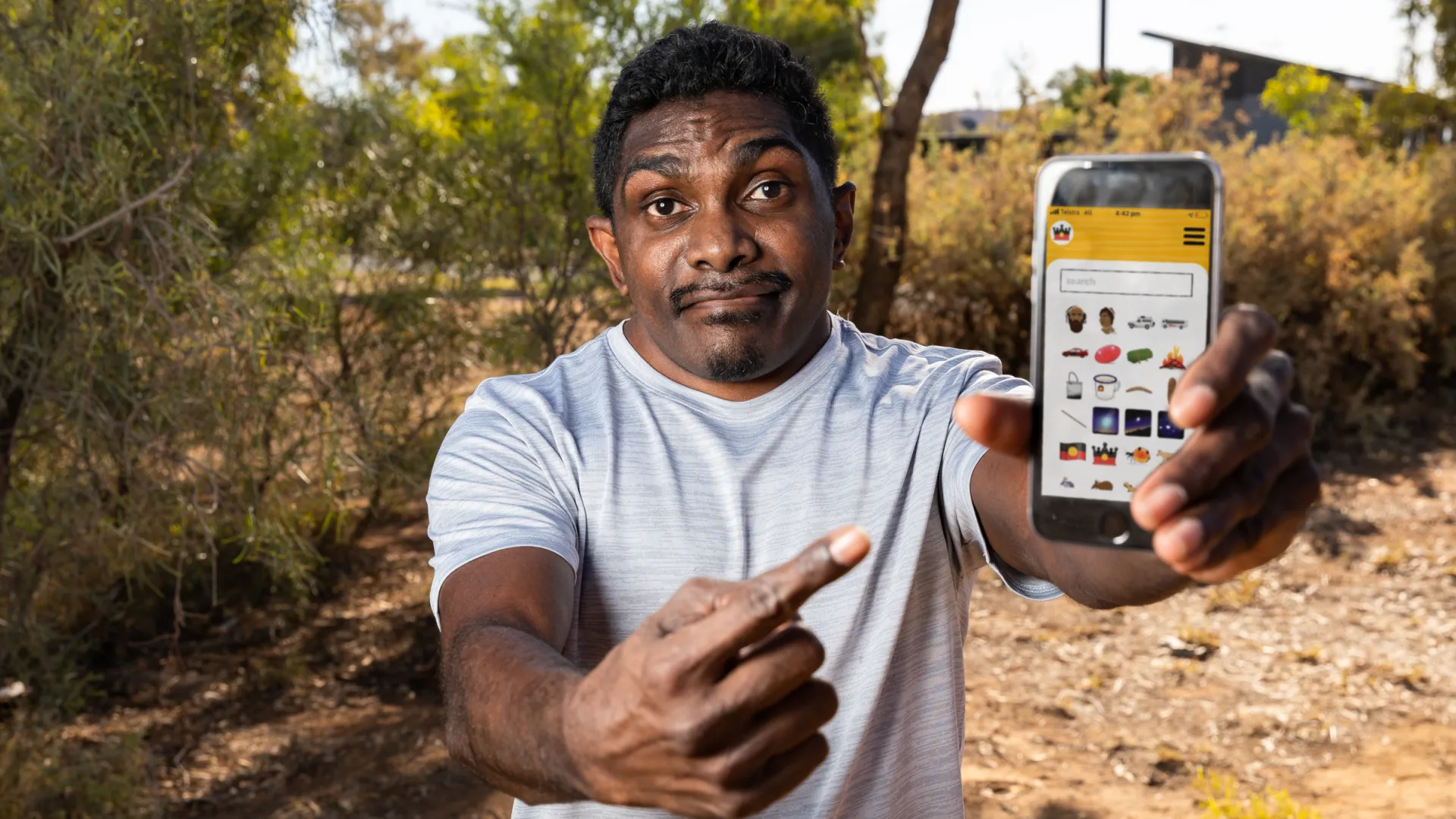 Man holding phone out to camera with Indigemoji app