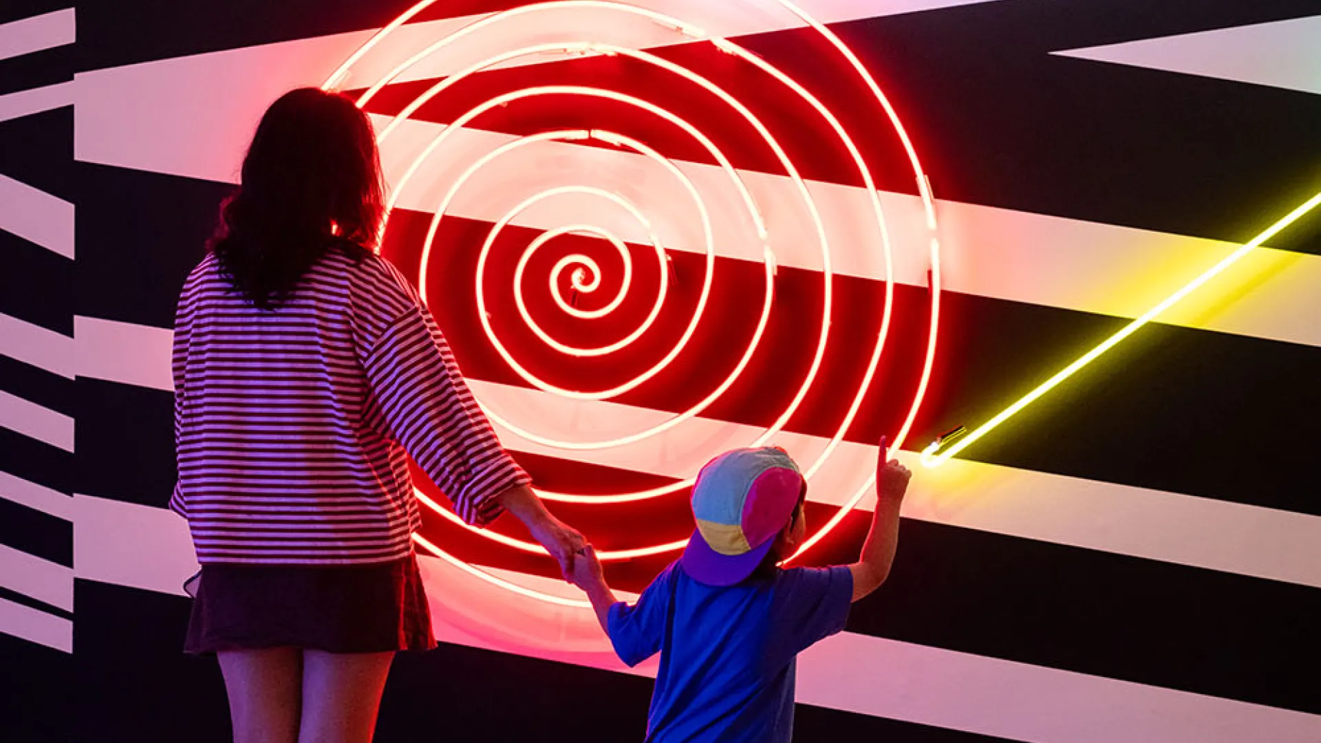 Woman and child standing in front of a neon artwork
